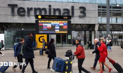 Passengers push luggage outside Terminal 3 as a gate information screen can be seen in the background
