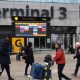 Passengers push luggage outside Terminal 3 as a gate information screen can be seen in the background