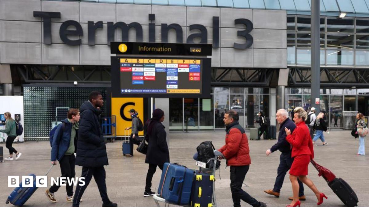 Passengers push luggage outside Terminal 3 as a gate information screen can be seen in the background