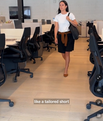 screenshot from NYT video on "how to elevate a basic white tee"; she is wearing tailored shorts and a sweater wrapped around her waist