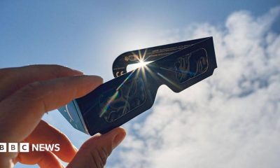 A pair of eclipse glasses held up in front of the sun