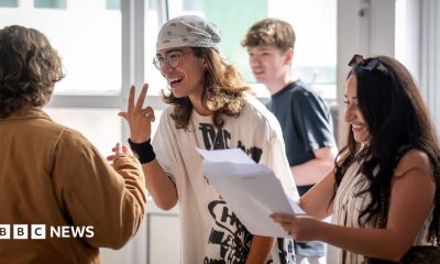 A group of students gather around holding papers and gesturing to each other while reading their results at a high school in Cardiff on Thursday.