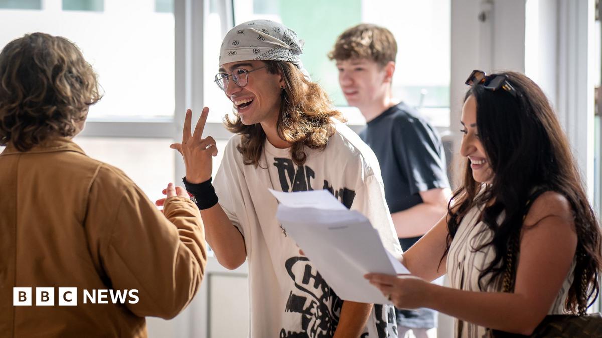 A group of students gather around holding papers and gesturing to each other while reading their results at a high school in Cardiff on Thursday.