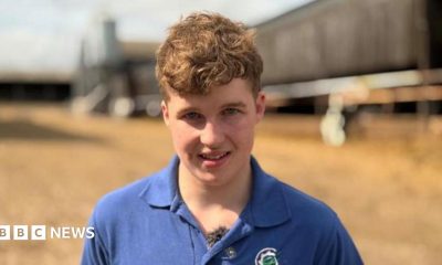 A young man is on a farm. There are sheds in the background.