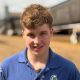 A young man is on a farm. There are sheds in the background.