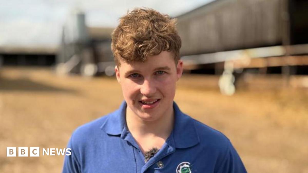 A young man is on a farm. There are sheds in the background.