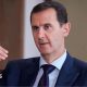 Bashar al-Assad pictured in 2016 speaking while gesturing with one hand. He is wearing a dark suit, white shirt and tie.