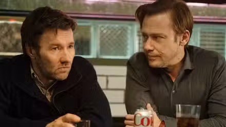 Joel Edgerton and Jimmie Simpson sit together at a bar with drinks, looking solemn