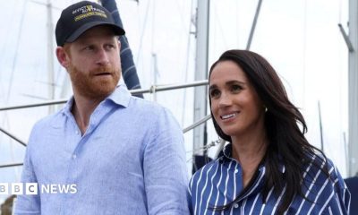 Harry and Meghan seen walking together in Sydney harbour in April. He is wearing a blue shirt and a cap, she is wearing a striped blue shirt.