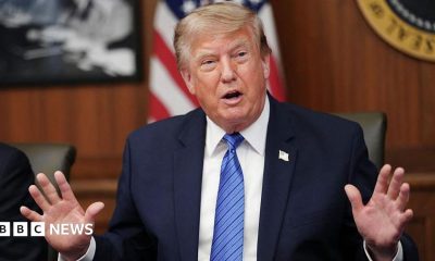 Donald Trump holds up his right fist while wearing a white shirt and red tie.