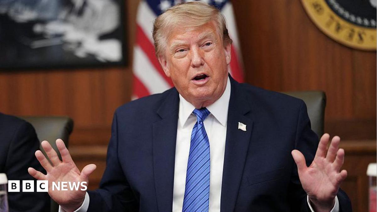 Donald Trump holds up his right fist while wearing a white shirt and red tie.