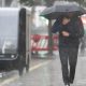 A man wearing a sodden jacket and trousers carries an umbrella down a street through a downpour