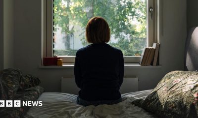 A woman looks out of a window while sitting on a bed.
