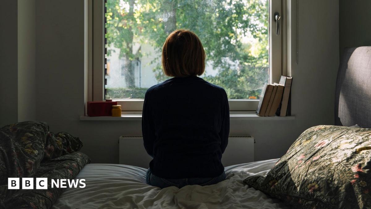 A woman looks out of a window while sitting on a bed.