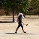 Person walking across a very dry and brown park with a towel over their head, providing shelter from the hot weather