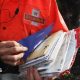 An employee of Royal Mail sorts parcels and letters in the back of his delivery van. The Royal Mail branding is on the back of his jacket and on the side of the van.