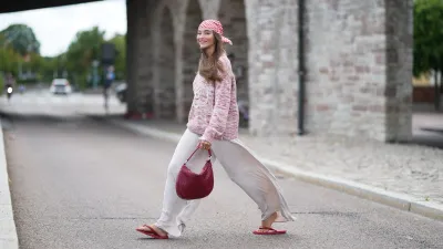 COPENHAGEN, DENMARK - JULY 06: Evi Wave wears a red and white check headscarf, long straight brown hair with a center part, a pink and white knit crew-neck sweater with long sleeves, cream white satin wide-leg pants, a burgundy woven shoulder bag, burgundy sandals shoes, outside Marimekko, during Copenhagen Fashion Week Spring/Summer 2027, on July 06, 2026 in Copenhagen, Denmark (Photo by Edward Berthelot/Getty Images)