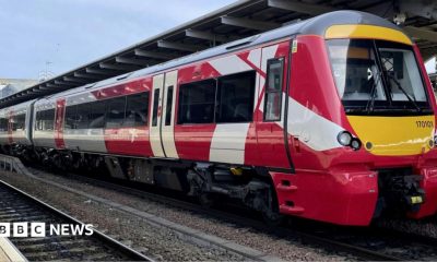 A red and white train is parked on railway tracks next to a train station.