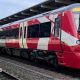 A red and white train is parked on railway tracks next to a train station.