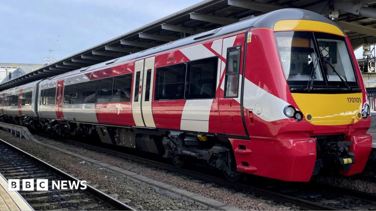 A red and white train is parked on railway tracks next to a train station.