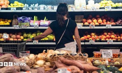 A woman looks at apples in a supermaket aisle.