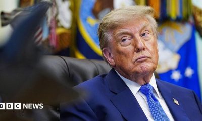 Donald Trump glances to his right while seated at his desk in the Oval Office.