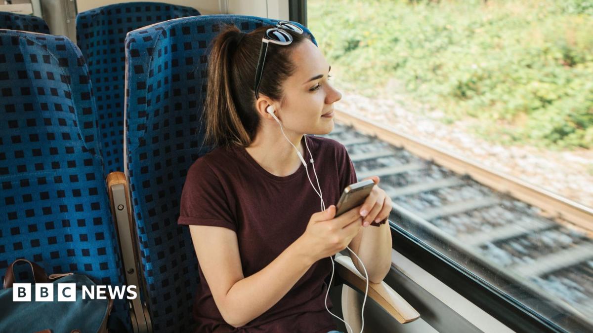 A teenage girl sitting on a train listening to headphones