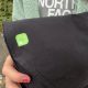 A close-up of a black pair of trousers. There is a green square sticker on them.