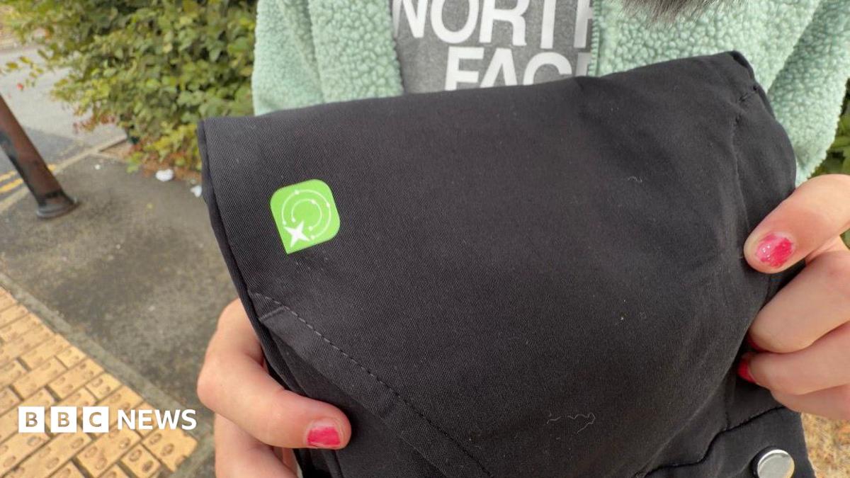 A close-up of a black pair of trousers. There is a green square sticker on them.