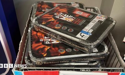 Disposable barbecues entitled "Put Me Out" piled up in a wire basket in a shop