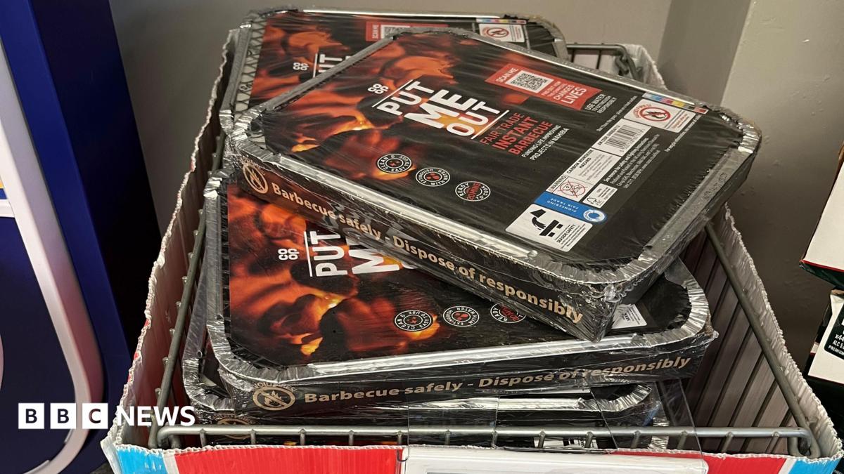 Disposable barbecues entitled "Put Me Out" piled up in a wire basket in a shop