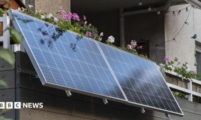 Infographic showing how plug-in solar panels work. A solar panel outside a house converts sunlight into direct current (DC) electricity, which passes through a microinverter that converts it to alternating current (AC). An AC cable then plugs into a standard household socket to help power the home.