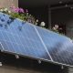 Infographic showing how plug-in solar panels work. A solar panel outside a house converts sunlight into direct current (DC) electricity, which passes through a microinverter that converts it to alternating current (AC). An AC cable then plugs into a standard household socket to help power the home.