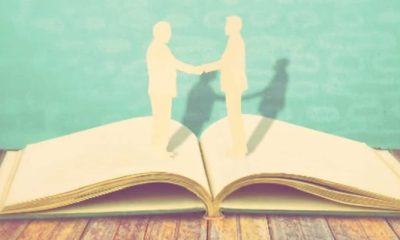 artistic rendering of two people shaking hands and possibly one is a woman building her book of business -- the figures look like cardboard cutouts sitting on top of an open book.