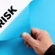To uncover hidden business risks concept. Male hand opens the blue paper and reveals the word risk.