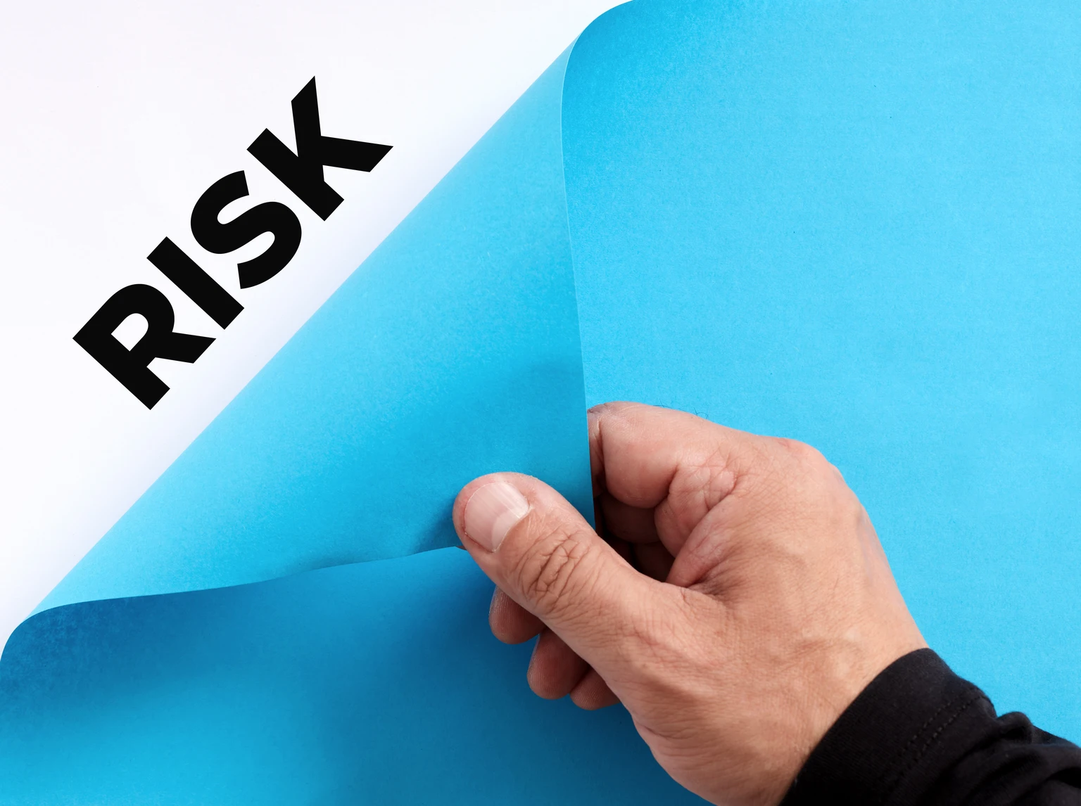 To uncover hidden business risks concept. Male hand opens the blue paper and reveals the word risk.