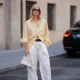 MUNICH, GERMANY - JULY 27: Lea Rohe is seen wearing a pale yellow oversized vintage cotton button front shirt; white wide leg linen trousers from Mango x Hailey Bieber; a black leather belt from The Horse; dark brown leather boat shoes with metal toggles from Longchamp; a small white structured leather top handle bag with silver tone hardware from Le Tanneur; rectangular black acetate sunglasses with dark tinted lenses from Corlin Eyewear on July 27, 2026 in Munich, Germany. (Photo by Moritz Scholz/Getty Images)