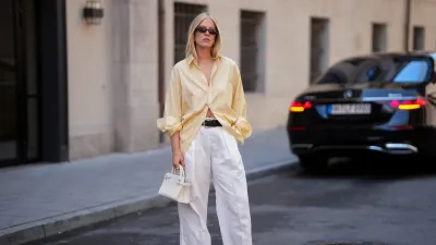 MUNICH, GERMANY - JULY 27: Lea Rohe is seen wearing a pale yellow oversized vintage cotton button front shirt; white wide leg linen trousers from Mango x Hailey Bieber; a black leather belt from The Horse; dark brown leather boat shoes with metal toggles from Longchamp; a small white structured leather top handle bag with silver tone hardware from Le Tanneur; rectangular black acetate sunglasses with dark tinted lenses from Corlin Eyewear on July 27, 2026 in Munich, Germany. (Photo by Moritz Scholz/Getty Images)