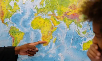 Black male's hand points to Africa on the world map as a black boy looks on from the side with his hand covering his mouth