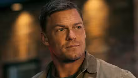 Alan Ritchson as Jack Reacher looks off camera with a blurred background in Reacher Season 2.