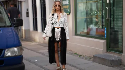 COPENHAGEN, DENMARK - AUGUST 3: A guest is seen wearing a white floral lace cropped cardigan with black floral appliqué detailing layered over a black bralette; ivory satin lace trim shorts; a sheer black lace wrap skirt; brown suede lace up sneakers with contrast stitching from Acne Studios; a white woven leather shoulder bag with black floral embellishments; white cat eye sunglasses; gold hoop earrings; and layered pendant necklaces during Day One of Copenhagen Fashion Week Spring/Summer 2027, outside the Modström by Prudence Davis event, on August 3, 2026 in Copenhagen, Denmark. (Photo by Moritz Scholz/Getty Images)