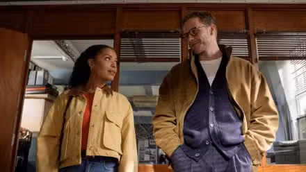 Antonia Thomas and Josh Dylan standing side-by-side and giving a knowing look in Tommy and Tuppence