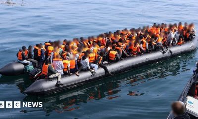 A large number of people in orange lifejackets on an inflatable boat.