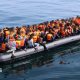 A large number of people in orange lifejackets on an inflatable boat.