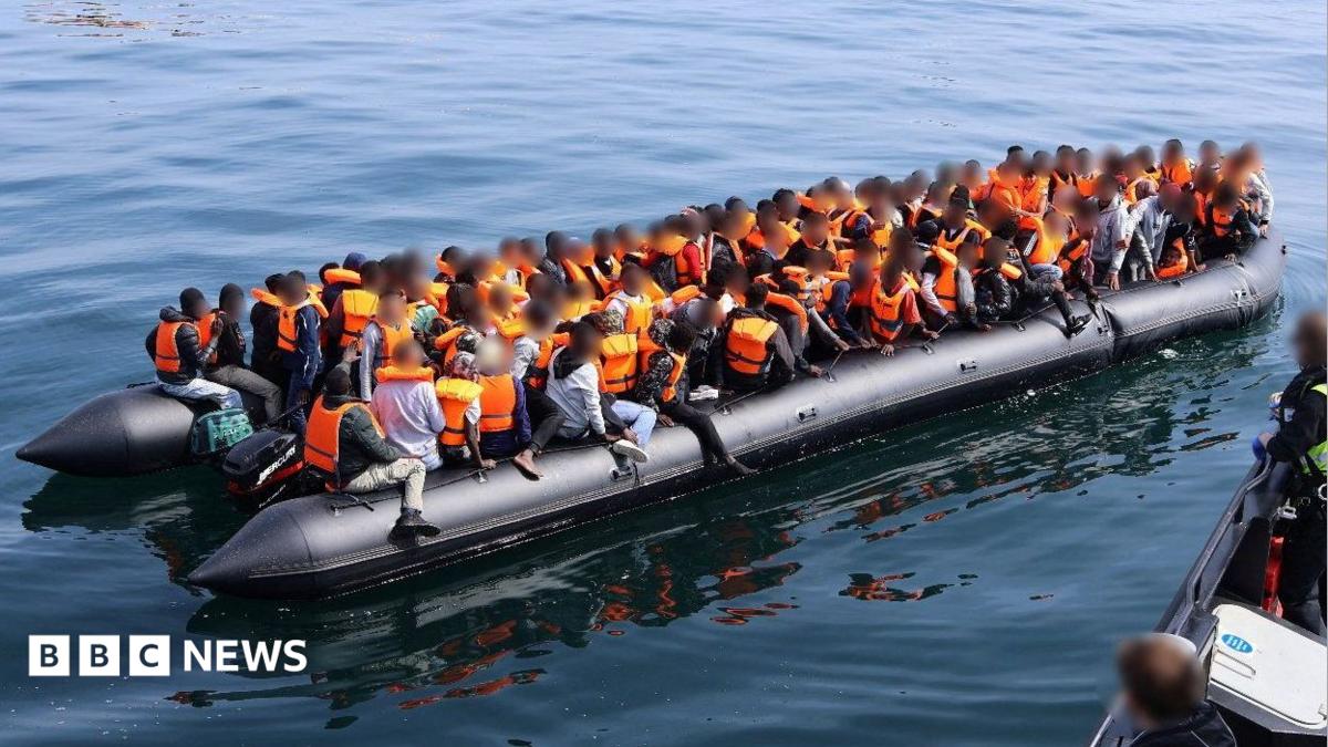 A large number of people in orange lifejackets on an inflatable boat.