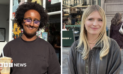 Hanad, wearing a glasses and a black T-shirt and holding an iced coffee, smiles as he stands outside a shop in London.