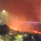 A fire in the basement of a hotel. Flames can be seen from below the building, and emergency services can be seen in the foreground.
