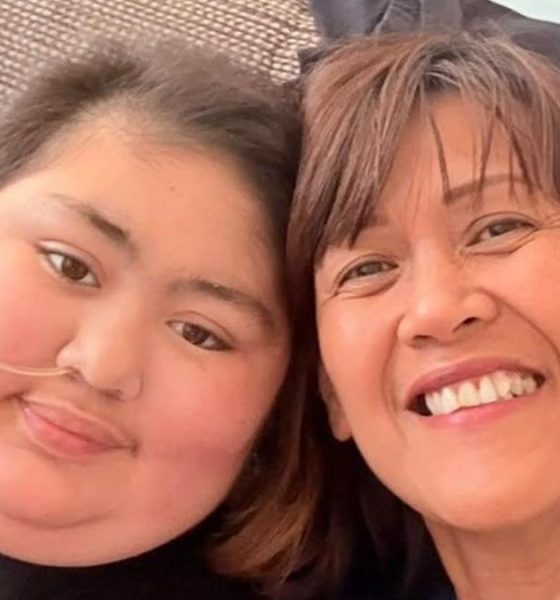 A woman and her daughter, sitting next to each other and smiling into a camera. The daughter, left, has short hair and has a tube inserted into her nose, which is taped to her face.