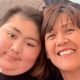 A woman and her daughter, sitting next to each other and smiling into a camera. The daughter, left, has short hair and has a tube inserted into her nose, which is taped to her face.