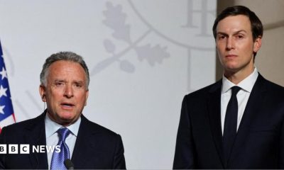 Steve Witkoff (left) and Jared Kushner (right) stand side by side looking directly towards the camera. They are both in black suits with white shirts. Witkoff has a blue patterned tie and Kushner has a black tie